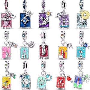 Könnte beinhalten: Eine Auswahl an silberfarbenen Charm-Anhängern mit Tarotkarten-Designs. Jeder Anhänger zeigt eine rechteckige Karte mit farbenfrohen Illustrationen und Texten wie "The Lovers", "The Star" und "The Sun". Die Charms sind mit verschiedenen Verzierungen versehen.