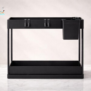 Könnte beinhalten: Ein schwarzes, zweistufiges Aufbewahrungsregal mit rechteckiger Basis und einem kleinen, angebrachten Behälter. Das Regal hat ein minimalistisches Design mit klaren Linien und einer matten Oberfläche. Der Text "FRESH LOOK by NATHAM" befindet sich in der oberen linken Ecke.