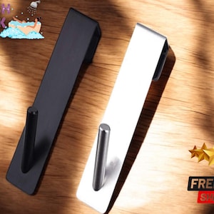 May include: Two modern over-the-door hooks, one black and one white, with a cylindrical hook. The hooks are displayed on a wooden surface. The image includes the text "FRESH LOOK" and "FREE SHIPPING".