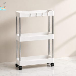 May include: A white, three-tiered rolling cart with chrome support poles. The cart has three shelves and four black wheels. The top shelf has hooks. The cart is designed for storage and organization.