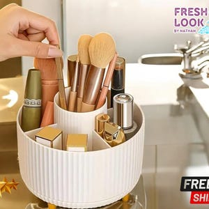 Puede incluir: Un organizador de maquillaje giratorio blanco con múltiples compartimentos, que contiene varios pinceles de maquillaje, barras de labios y otros productos de belleza. El organizador tiene un exterior acanalado y está sobre una superficie amarilla. Incluye el texto "FRESH LOOK BY NATHAN".