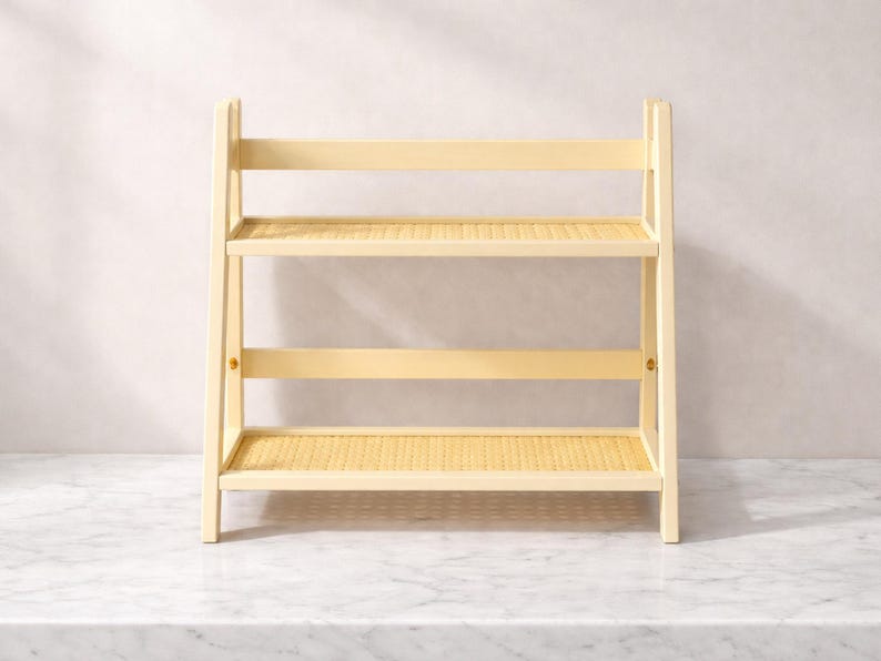 May include: A light-colored, two-tiered wooden shelf with woven rattan shelves. The shelf has a rectangular shape and is supported by four legs. The shelves are ideal for displaying decorative items or organizing small objects.