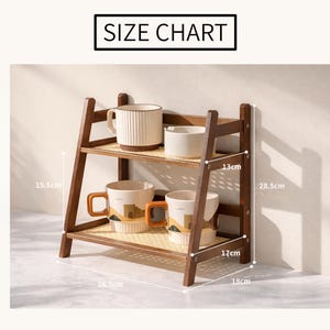 May include: A two-tiered wooden shelf with a woven base, holding cream-colored mugs and bowls. The shelf is 18 inches wide, 17 inches deep, and 28.5 cm tall. The top shelf is 13 cm from the top. The text "SIZE CHART" is at the top.