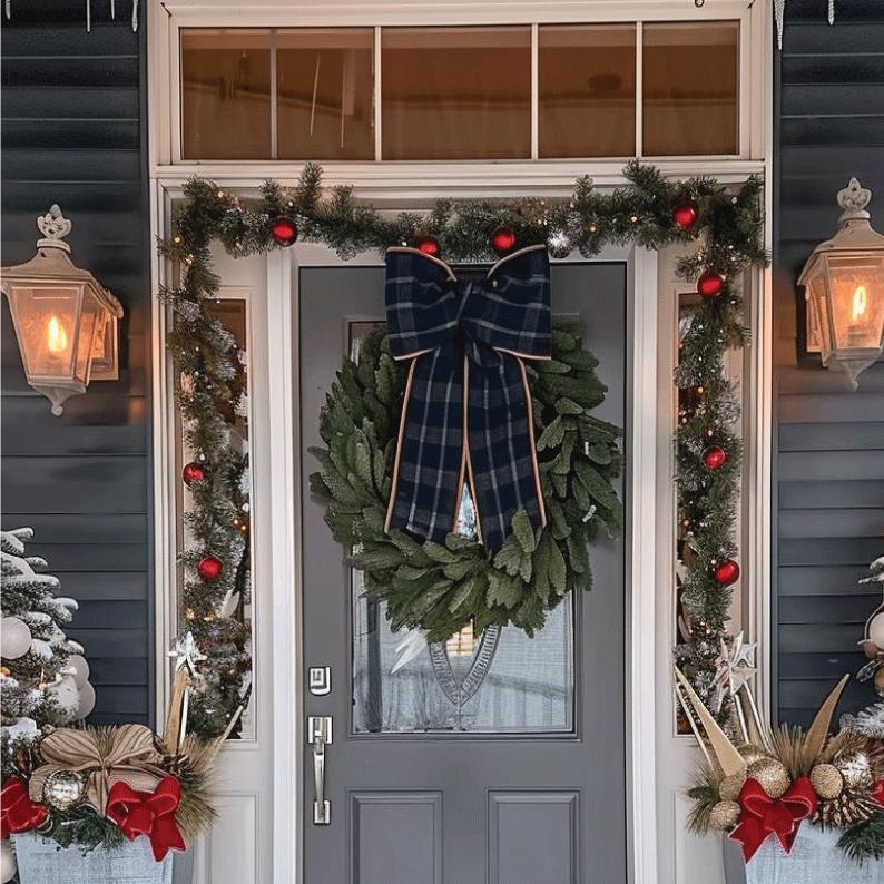 Puede incluir: Una puerta de entrada decorada para Navidad con una corona verde, un lazo a cuadros y guirnalda con adornos rojos. La puerta es gris y la casa tiene revestimiento azul. Dos faroles iluminados flanquean la puerta.