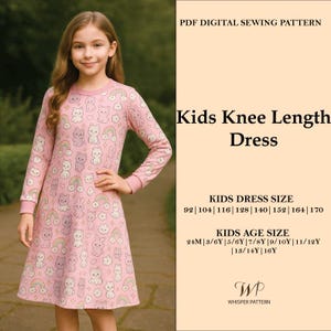 Op de afbeelding: Een meisje draagt een roze knielange jurk met een patroon van cartoonkatten, konijnen en regenbogen. De jurk met lange mouwen maakt deel uit van een digitaal PDF-naaipatroon voor kinderen. Tekst aan de rechterkant geeft maten aan.