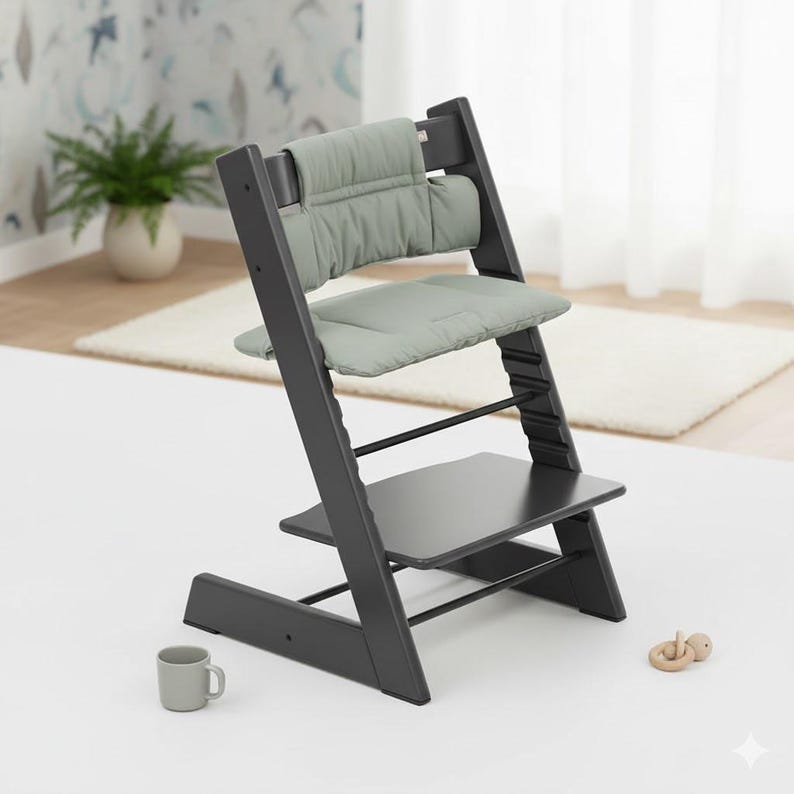 Puede incluir: Una silla alta de madera gris oscuro con un coj&iacute;n acolchado para el asiento y el respaldo en color verde salvia. La silla tiene un dise&ntilde;o ajustable con m&uacute;ltiples ranuras a lo largo de los soportes laterales, base plana y reposapi&eacute;s.