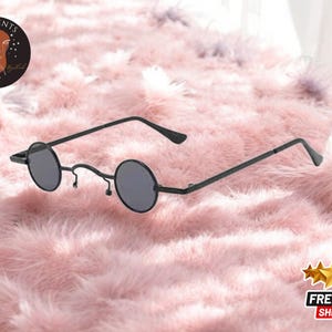 May include: Black round-framed glasses with thin metal arms. The glasses are on a pink fluffy surface.