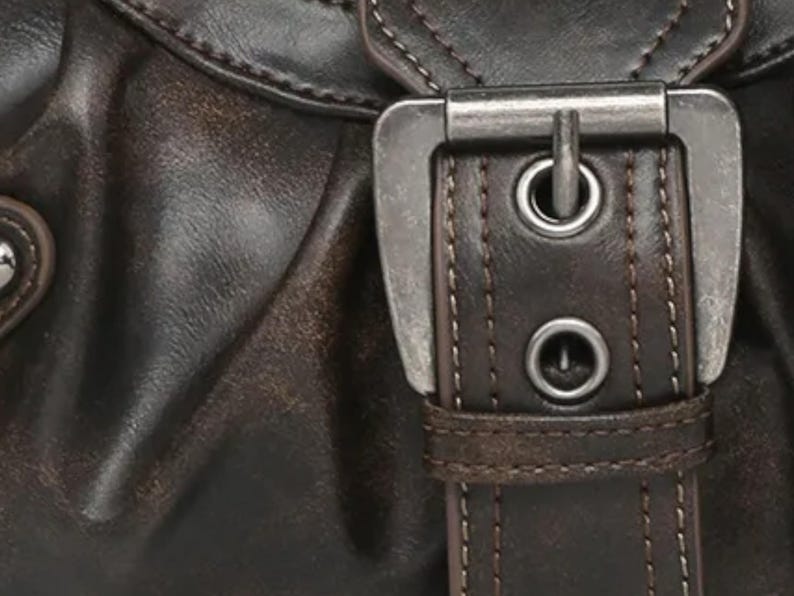 May include: Close-up of a brown leather bag with a silver buckle and stitching. The buckle has two metal eyelets.