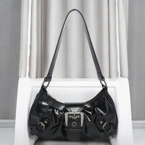 May include: A black leather handbag with a silver buckle and a single strap. The bag has a curved shape and a glossy finish.