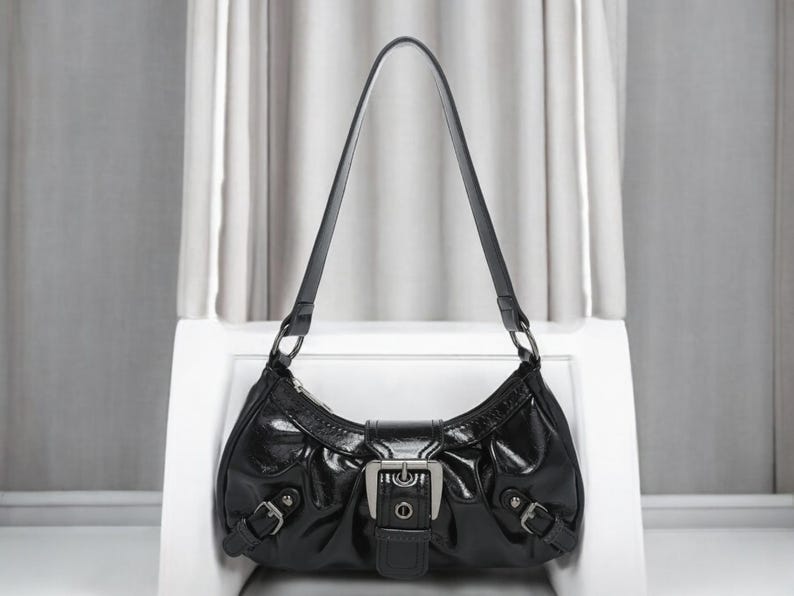 May include: A black leather handbag with a silver buckle and a single strap. The bag has a curved shape and a glossy finish.