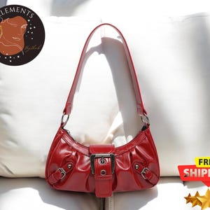 May include: A red leather handbag with a silver buckle and a short strap. The bag has a curved shape and a slightly slouchy look.