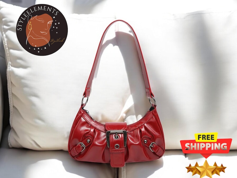 May include: A red leather handbag with a silver buckle and a short strap. The bag has a curved shape and a slightly slouchy look.