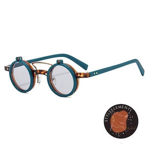 May include: Round teal and tortoise shell eyeglasses with gray lenses. The glasses have a unique design with teal arms and a bridge. The lenses are set in a circular frame. The glasses are a stylish accessory.