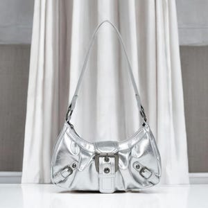 May include: A silver metallic handbag with a buckle closure and a single strap.