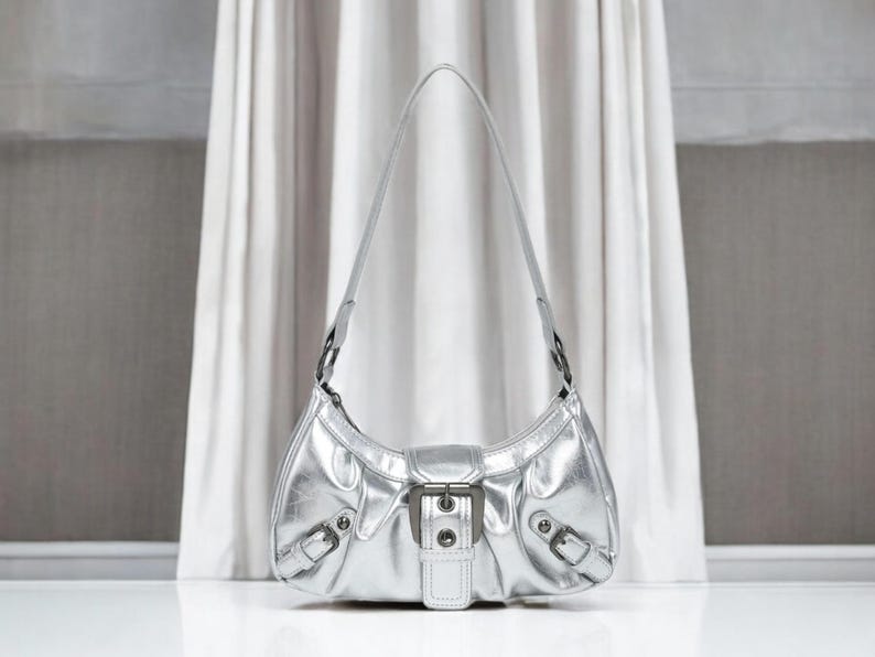 May include: A silver metallic handbag with a buckle closure and a single strap.