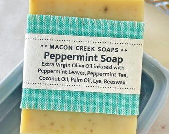 May include: A bar of peppermint soap wrapped in a green and white checkered fabric with a label that reads "MACON CREEK SOAPS.. Peppermint Soap Extra Virgin Olive Oil infused with Peppermint Leaves, Peppermint Tea, Coconut Oil, Palm Oil, Lye, Beeswax"