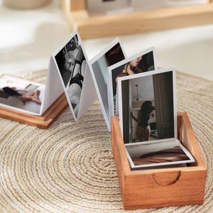 May include: A wooden photo display featuring a series of intimate black and white and color photographs. The display is open, revealing several images, and is set on a woven mat. A wooden calendar is in the background.