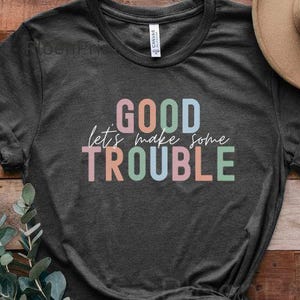 May include: A dark gray t-shirt with the text "GOOD let's make some TROUBLE" in colorful letters.