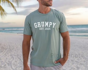 Może przedstawiać: Jasnozielony t-shirt z napisem "GRUMPY EST. 2025" w kolorze białym.