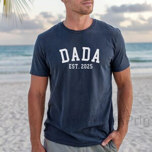 May include: A navy blue t-shirt with white text that reads "DADA EST. 2025".