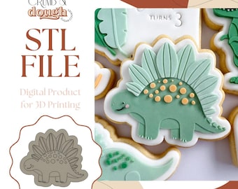 May include: An image featuring a green dinosaur cookie with yellow accents and a white outline. The cookie is decorated with a detailed design. The image also includes the text "STL FILE" and "Digital Product for 3D Printing".