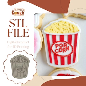 Peut inclure: Un fichier STL numérique pour l'impression 3D d'un emporte-pièce en forme de seau de popcorn. Le seau est rouge et blanc avec les mots "POP CORN" en cercle sur le devant. L'emporte-pièce est présenté à côté d'un biscuit décoré avec le même design.