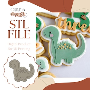 Puede incluir: Galleta de dinosaurio verde con glaseado blanco y detalles amarillos. La galleta presenta un diseño de dinosaurio amigable. La imagen incluye el texto "STL FILE" y "Digital Product for 3D Printing".