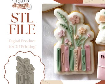 May include: A decorated cookie in the shape of a stack of books with flowers on top. The cookie is white with pink, green, and peach accents. The image also includes the text "STL FILE" and "Digital Product for 3D Printing".