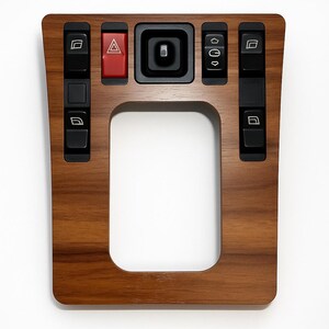 Può includere: Un pannello di console per auto in legno con una cornice rettangolare e vari pulsanti neri. Il pannello presenta un pulsante rosso per le luci di emergenza e i pulsanti di controllo dei finestrini. Il legno ha una calda tonalità marrone.