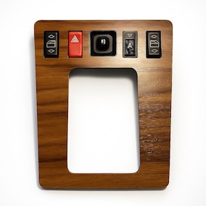 Könnte beinhalten: Holz-Autokonsole mit rechteckiger Öffnung und mehreren schwarzen Knöpfen. Die Knöpfe umfassen Fensterheber, einen roten Warnblinklichtschalter und andere Schalter. Das Holz hat eine warme, braune Maserung.