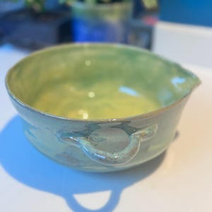 Peut inclure: Un bol en céramique fait à la main avec un intérieur vert clair et jaune et un extérieur bleu-vert. Le bol a deux poignées et un bec verseur. Le bol mesure environ 10 cm de diamètre et 8 cm de hauteur.
