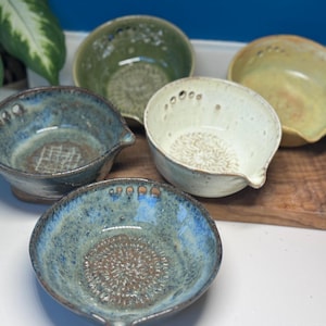 May include: A set of three ceramic mugs with a speckled, matte finish. The mugs are in shades of cream, light gray, and dark gray. Each mug has a simple, minimalist design, perfect for coffee or tea.