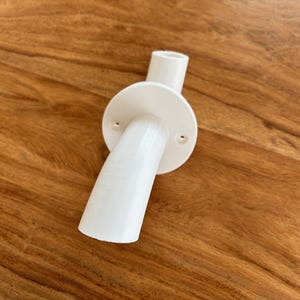May include: White plastic pipe fitting with a curved outlet and a round base with two screw holes.