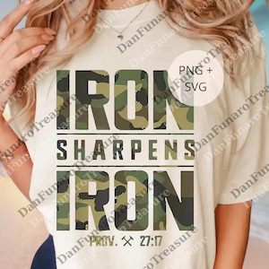 May include: A cream-coloured t-shirt featuring the text "IRON SHARPENS IRON" in a camouflage pattern. The text is in a bold, blocky font. The bottom of the shirt has the text "PROV. 27:17" with a hammer and pickaxe symbol.