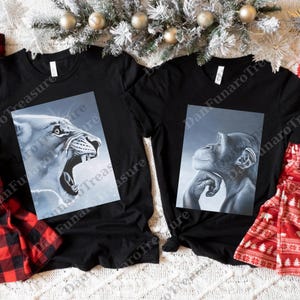May include: Two black t-shirts with animal portraits. One shirt features a roaring lion in shades of gray, and the other displays a thoughtful chimpanzee. The shirts are decorated with a festive holiday theme.