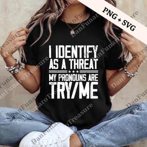 May include: Black t-shirt with the text "I IDENTIFY AS A THREAT, MY PRONOUNS ARE TRY/ME" in white block letters. The shirt has a crew neck and is worn with blue jeans and white sneakers. The image also includes the text "PNG + SVG".