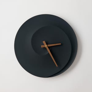 Puede incluir: Un reloj de pared negro con un diseño en espiral único y agujas de madera.