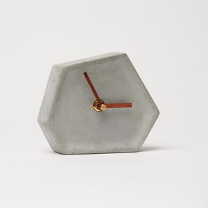 May include: A gray concrete hexagonal clock with wooden hands and gold accents.