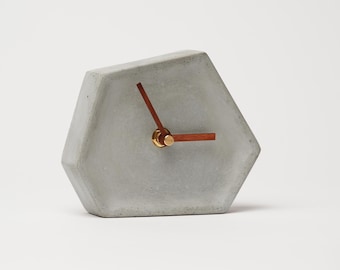 May include: A gray concrete hexagonal clock with wooden hands and gold accents.