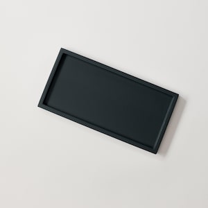 Può includere: Un vassoio rettangolare nero con un bordo leggermente rialzato. Il vassoio è realizzato in un materiale liscio e opaco.