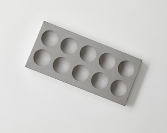 May include: A gray concrete tray with ten round cutouts. The tray is rectangular and has a smooth surface.