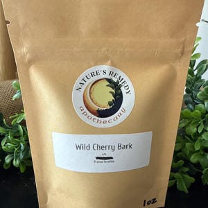 May include: A brown paper bag with a white label that reads "Wild Cherry Bark" and "Prunus Serotina". The bag has a circular sticker with the words "Nature's Remedy Apothecary". The bag is labeled "1 oz".