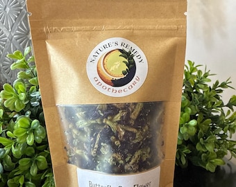 Peut inclure: Un sachet en papier brun avec une fenêtre transparente montrant de la fleur de pois papillon séchée. Le sachet a une fermeture en bois et une étiquette circulaire avec le texte "NATURE'S REMEDY apothecary". L'étiquette indique "Butterfly Pea Flower" et "whole".