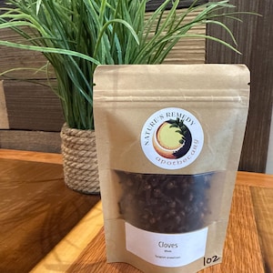 May include: A brown kraft paper stand-up pouch containing whole cloves. The label features the text Nature's Remedy Apothecary, Cloves, Whole, Syzygium aromaticum, and the number 102. A clear window reveals the dark brown dried cloves inside.