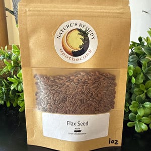 May include: A brown paper bag with a clear window displaying whole flax seeds. The bag has a circular sticker with the text "Nature's Remedy apothecary". Below the window is a white label with the words "Flax Seed Whole Linum Usitatissimum".