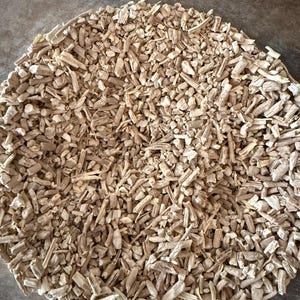 May include: A close-up shot of a pile of small, light brown, irregularly shaped pieces. The pieces appear to be dried, possibly wood or plant material, and are scattered across the surface.