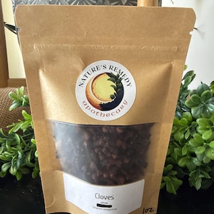 May include: A brown paper bag with a clear window, filled with whole cloves. The bag has a label that reads "Nature's Remedy apothecary" and "Cloves". The bag is labeled as 1 oz.