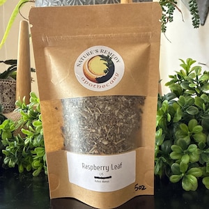 May include: A brown paper bag with a clear window displaying dried raspberry leaf. The bag has a white label with the text "Raspberry Leaf" and "Rubus idaeus". The bag also has a sticker with the text "Nature's Remedy Apothecary". The bag contains 5 oz of product.
