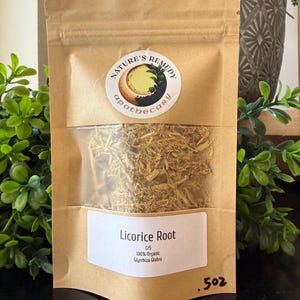 May include: A brown paper bag with a clear window, filled with dried licorice root. The bag has a circular sticker with the words "Nature's Remedy Apothecary". A white label reads "Licorice Root" and "100% Organic Glycyrrhiza Glabra". The bag contains .5 oz of licorice root.