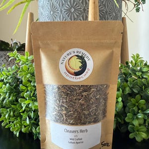 May include: A brown paper bag labeled "Nature's Remedy Apothecary" containing Cleavers Herb. The bag has a clear window showing dried herbs. The label also includes "Wild Crafted Galium Aparine" and the weight, .5 oz.